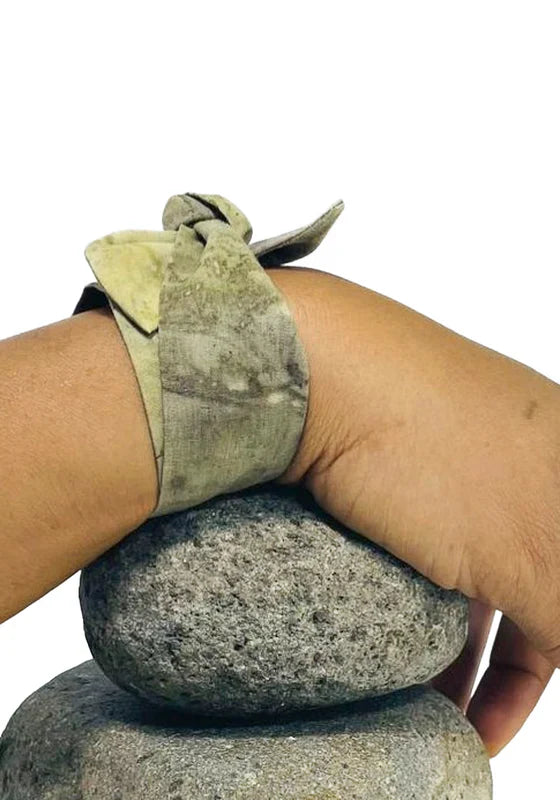 KaliZ Ruban Petit foulard coton Vegetal Skin — Exploration I, Trace XIII coloris Golden Mango-noir-vert, porté autour du poignet posé sur deux pierres, teinture végétale  à base de mangue - MURIELL Z Guadeloupe 